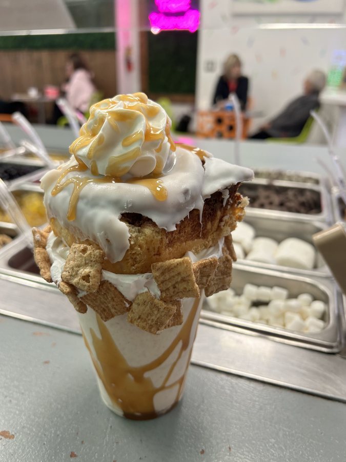 A caramel-drizzled soft serve stacked with cinnamon cereal over the topping bar at BerryVille